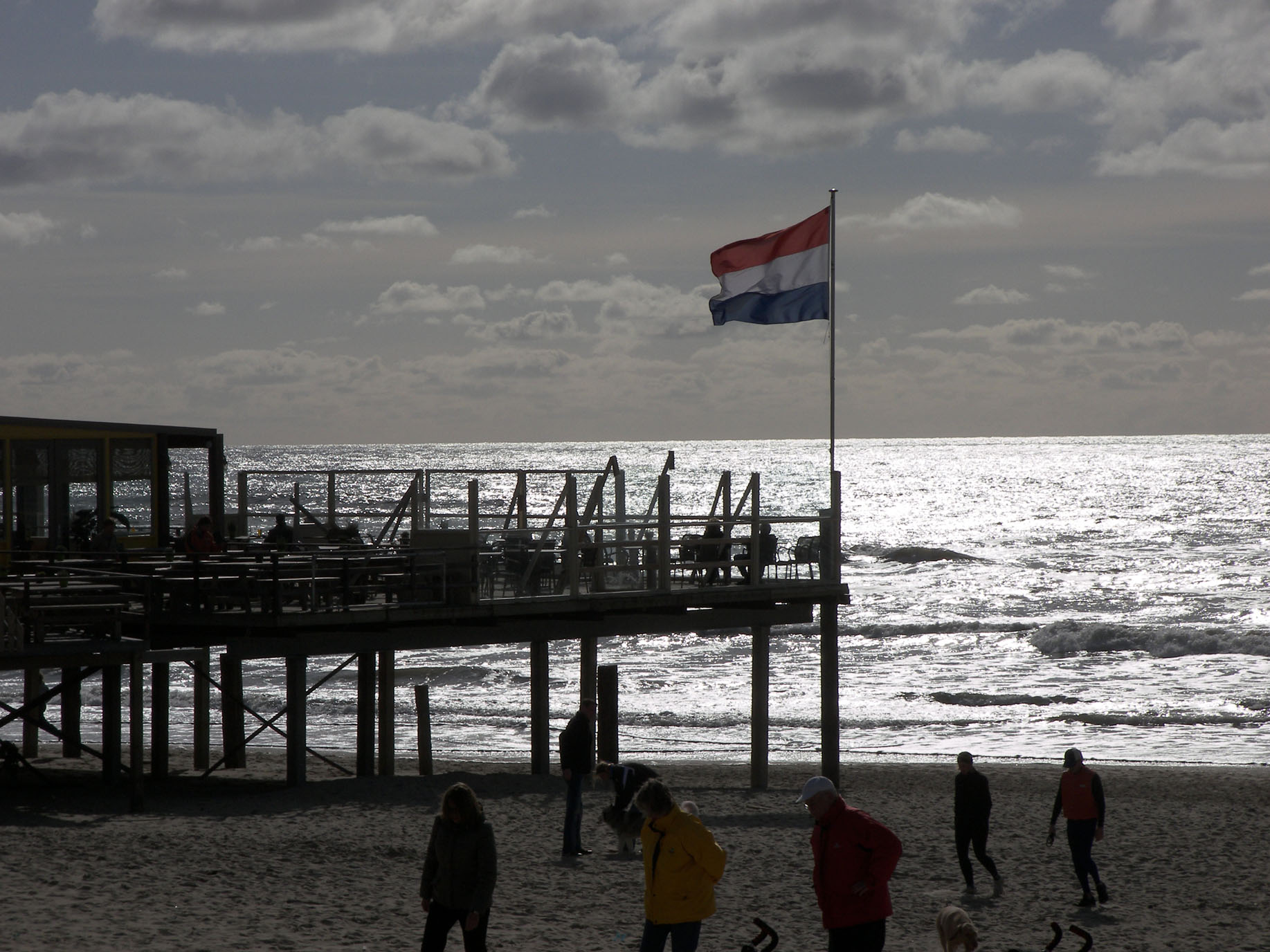 100_1677_Omgeving_2K_Q8 Foto strand met ondergaande zon. Strand paviljoen met Nederlandse vlag.