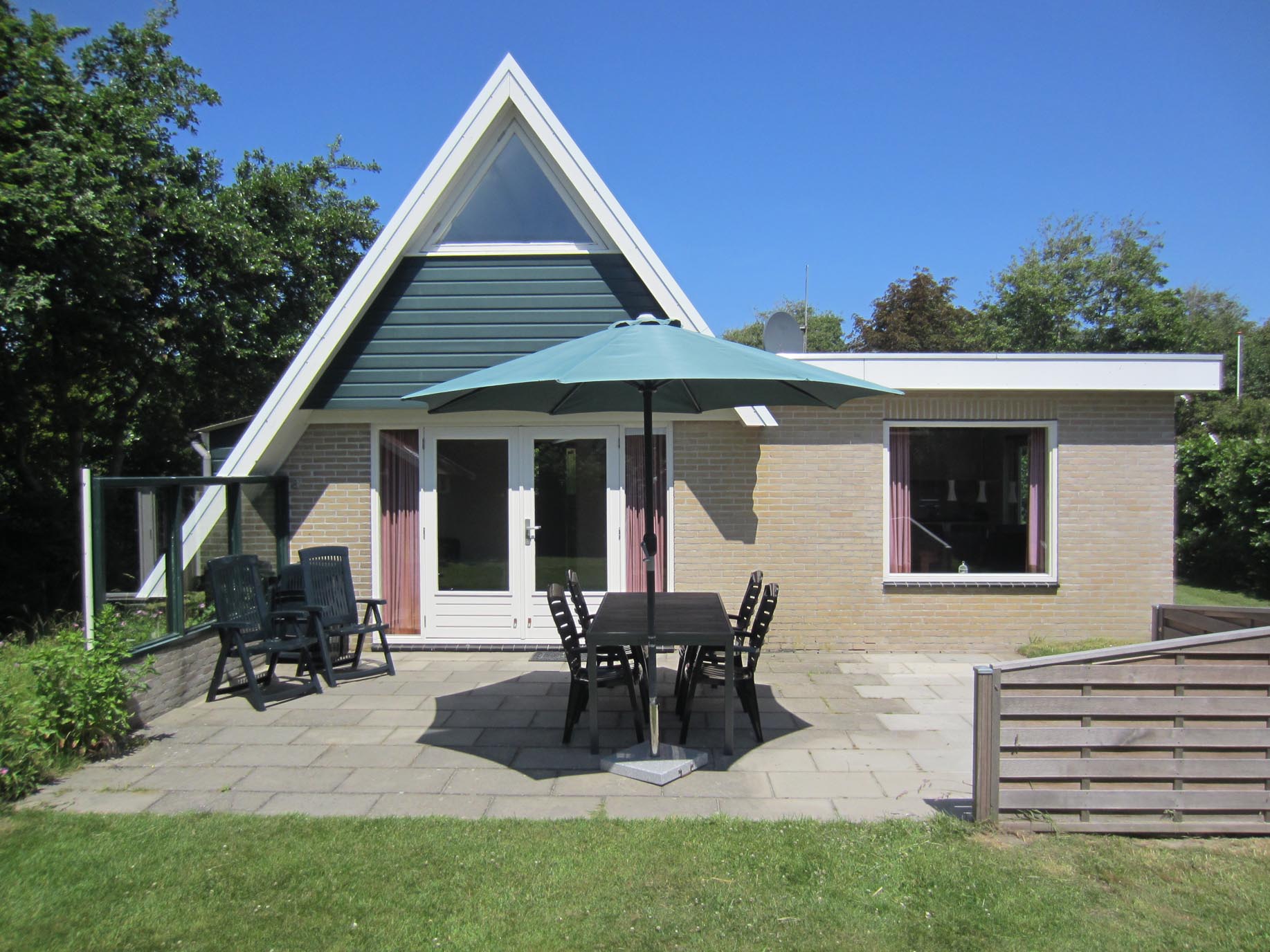 Sandepark 69. Stenen huis met uitbouw. Openslaande deuren naar het ruime terras met tuinstoelen en parasol.
