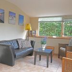 Sandepark 88. Zithoek in de woonkamer. Leren bank met 2 rieten stoelen. Salontafel met bosje bloemen.