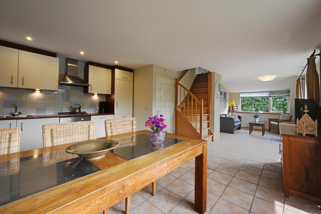 Sandepark 88. Overzichtsfoto woonkamer met vaste trap naar de verdieping, 6 persoons eettafel en keuken. Op de achtergrond de zithoek met bank en 2 stoelen.